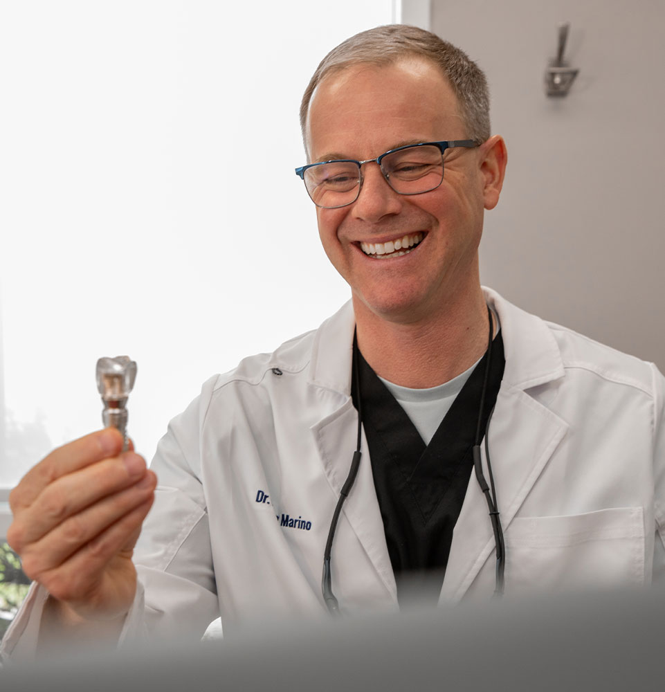 Dr. Marino smiling while holding a dental implant model in the Montville office